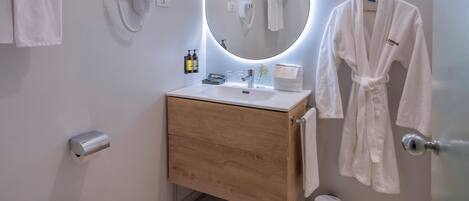A modern bathroom with a wooden vanity, a round mirror, a toilet, and a hand dryer.