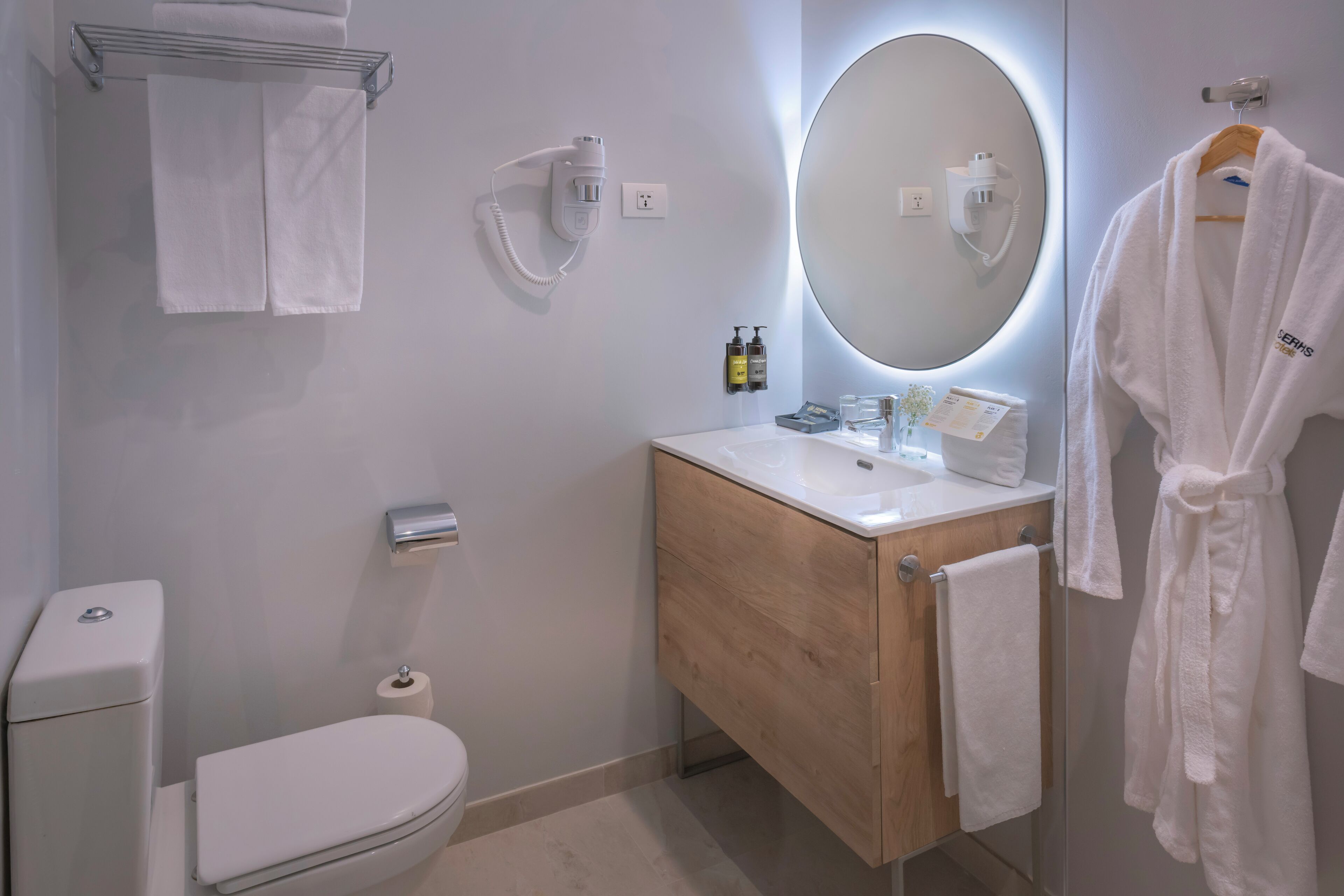 A modern bathroom with a toilet, sink, and mirror. There are towels and toiletries on the sink.