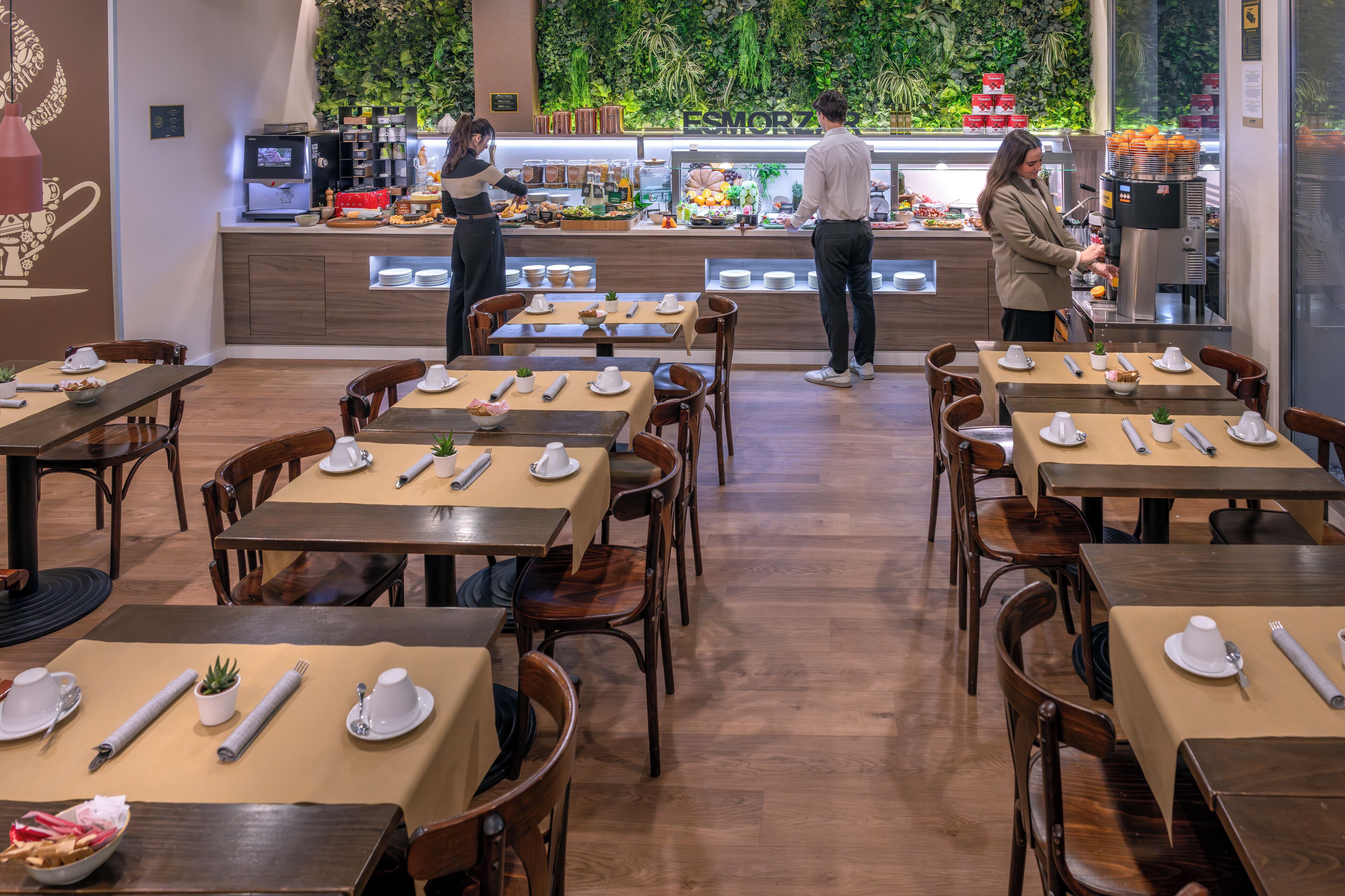 Un restaurant avec des tables dressées pour le service, un buffet en arrière-plan et un membre du personnel qui sert les plats.