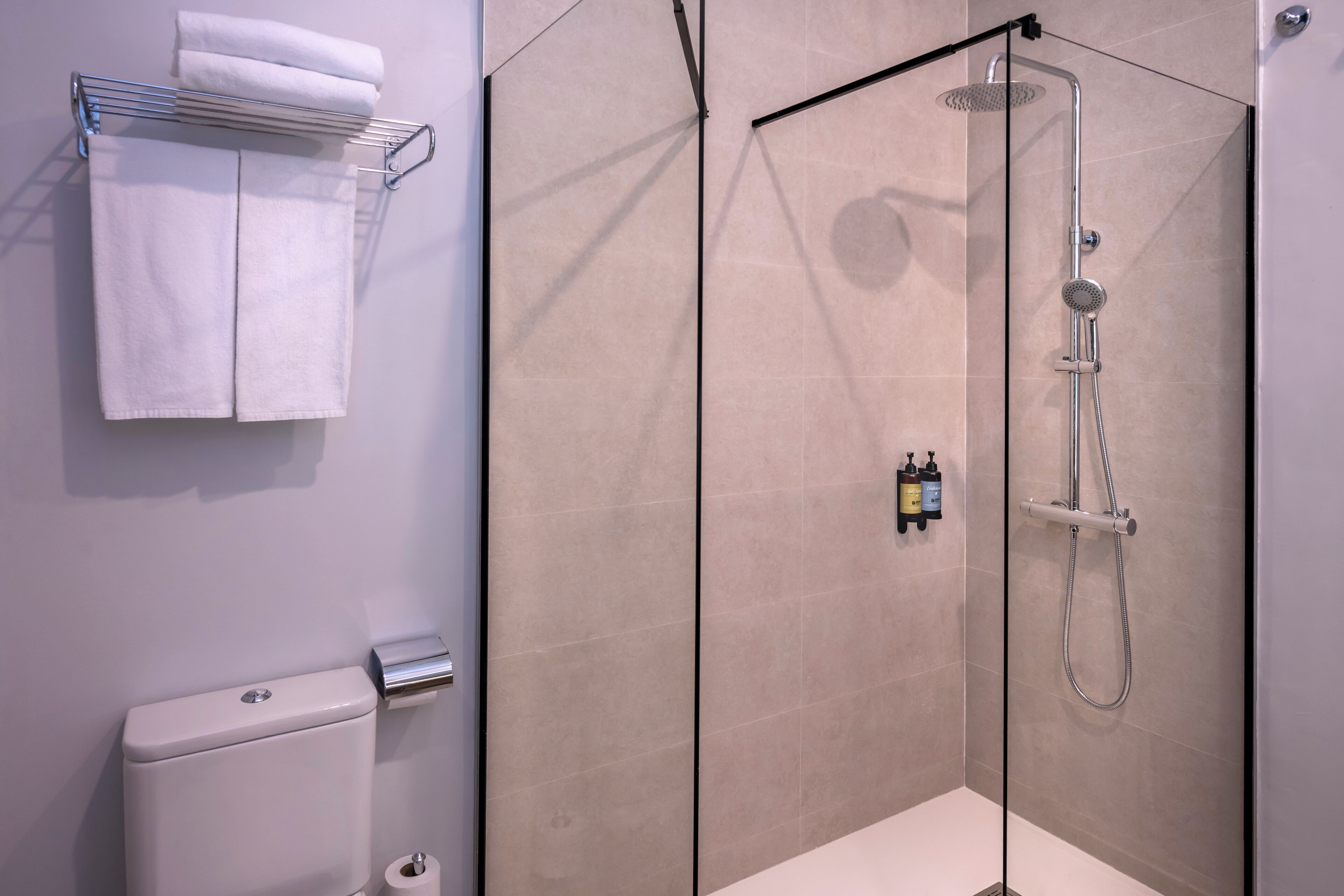A modern bathroom with a glass-enclosed shower, a toilet, and a towel rack with folded towels.