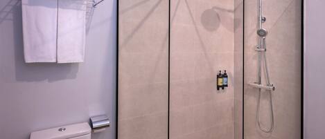 A modern bathroom with a glass-enclosed shower, a toilet, and a towel rack with folded towels.