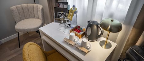 Habitación de hotel con un escritorio de madera, una silla, una lámpara, un hervidor de agua y una mesita con artículos de aseo.
