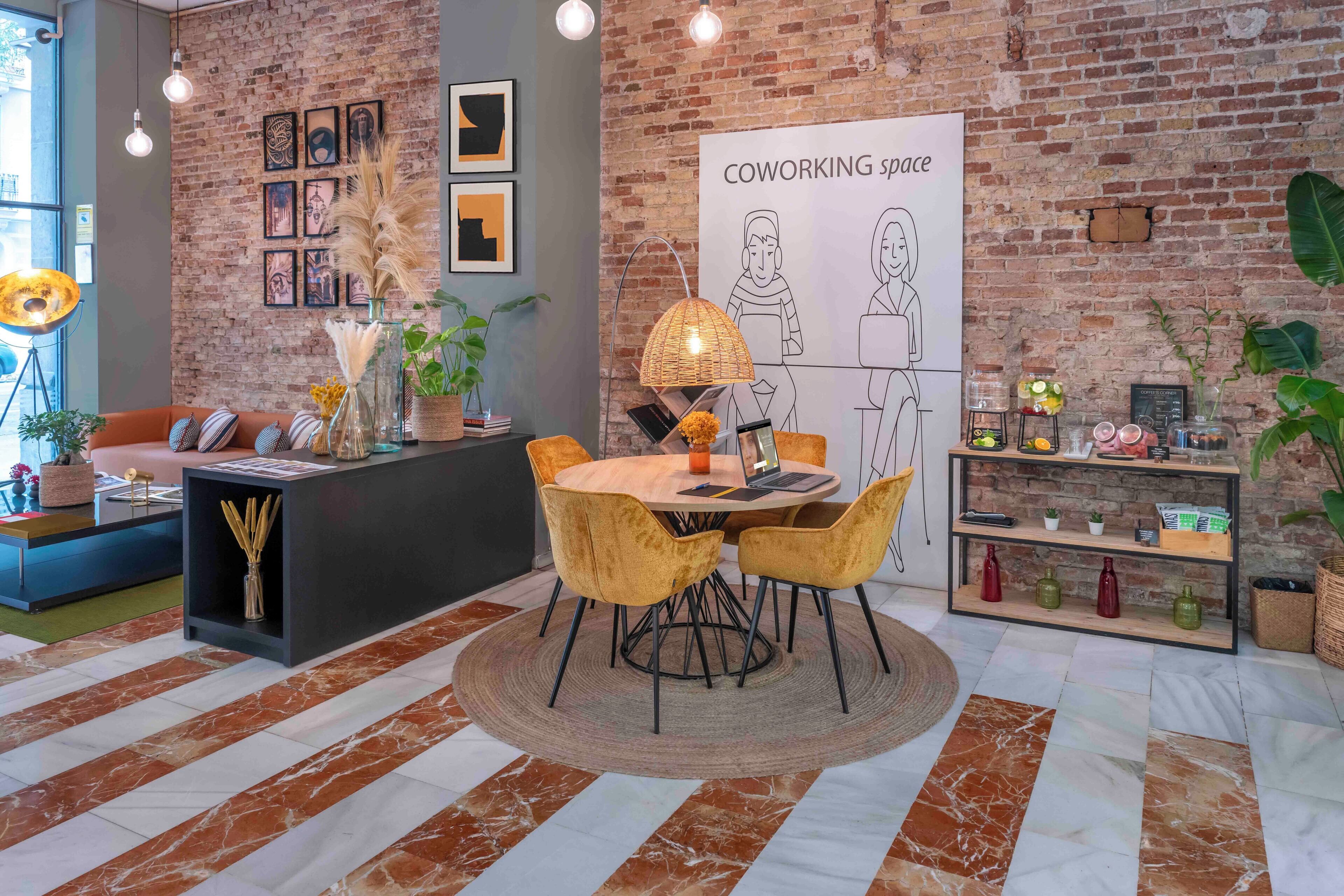 Un espacio de coworking con pared de ladrillo, una mesa redonda con sillas, un sofá y una estantería con varios objetos.
