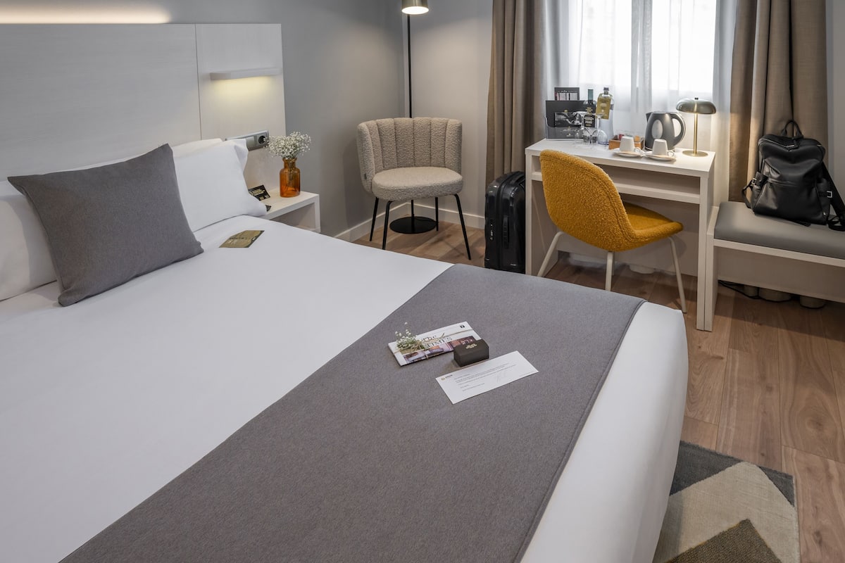 A hotel room with a bed, a desk, a chair, and a suitcase.
