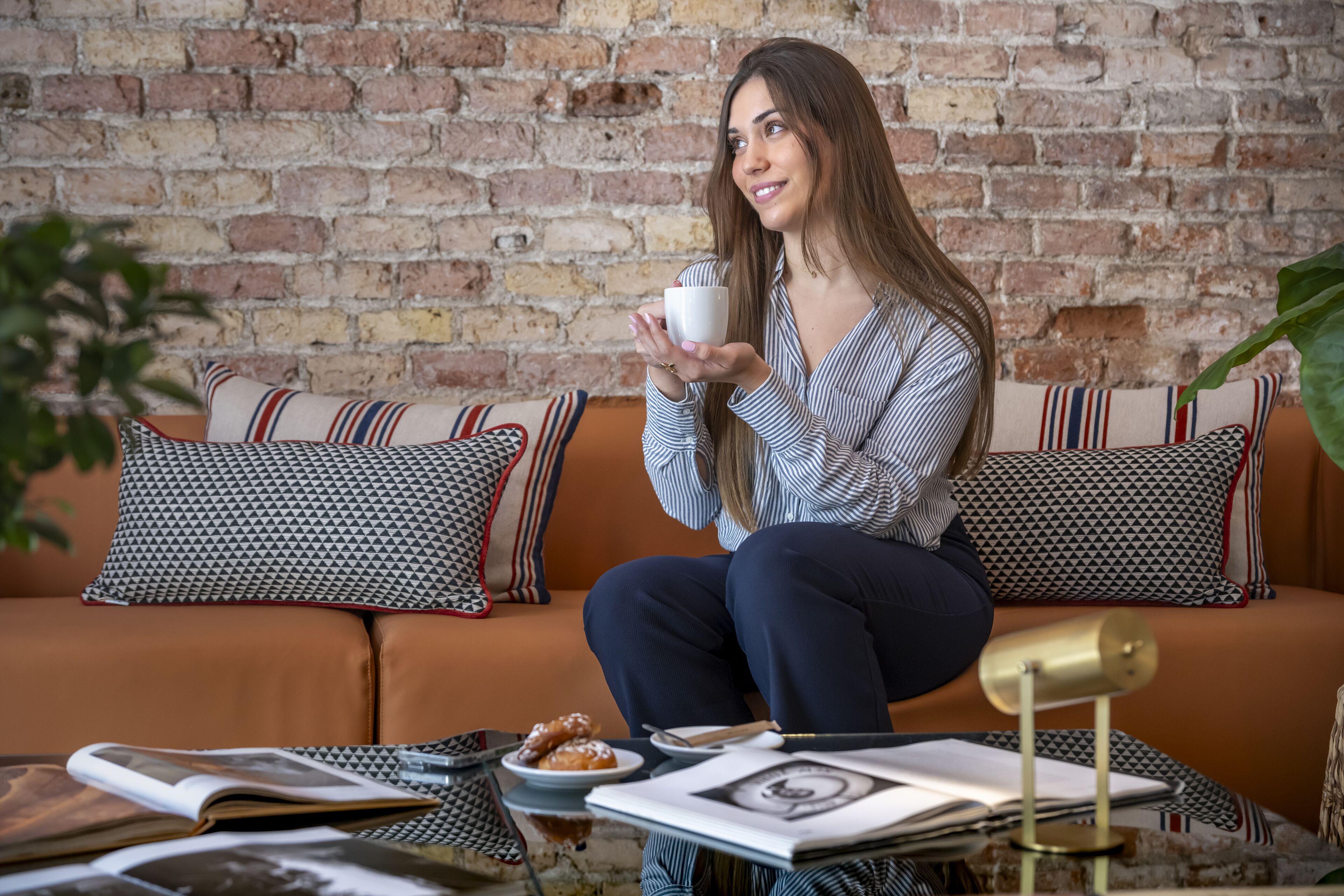 A person sitting on a sofa with patterned cushions, holding a cup.