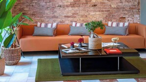 Una sala de estar acogedora con pared de ladrillo, un sofá con cojines estampados, una mesa de centro con adornos y lámparas colgantes.