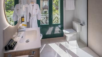 Un bany modern amb un lavabo ampli, un vàter i una dutxa. Hi ha una finestra amb vista a un balcó.