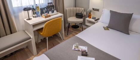 A hotel room with a bed, a desk, a chair, a bedside table, and a lamp.