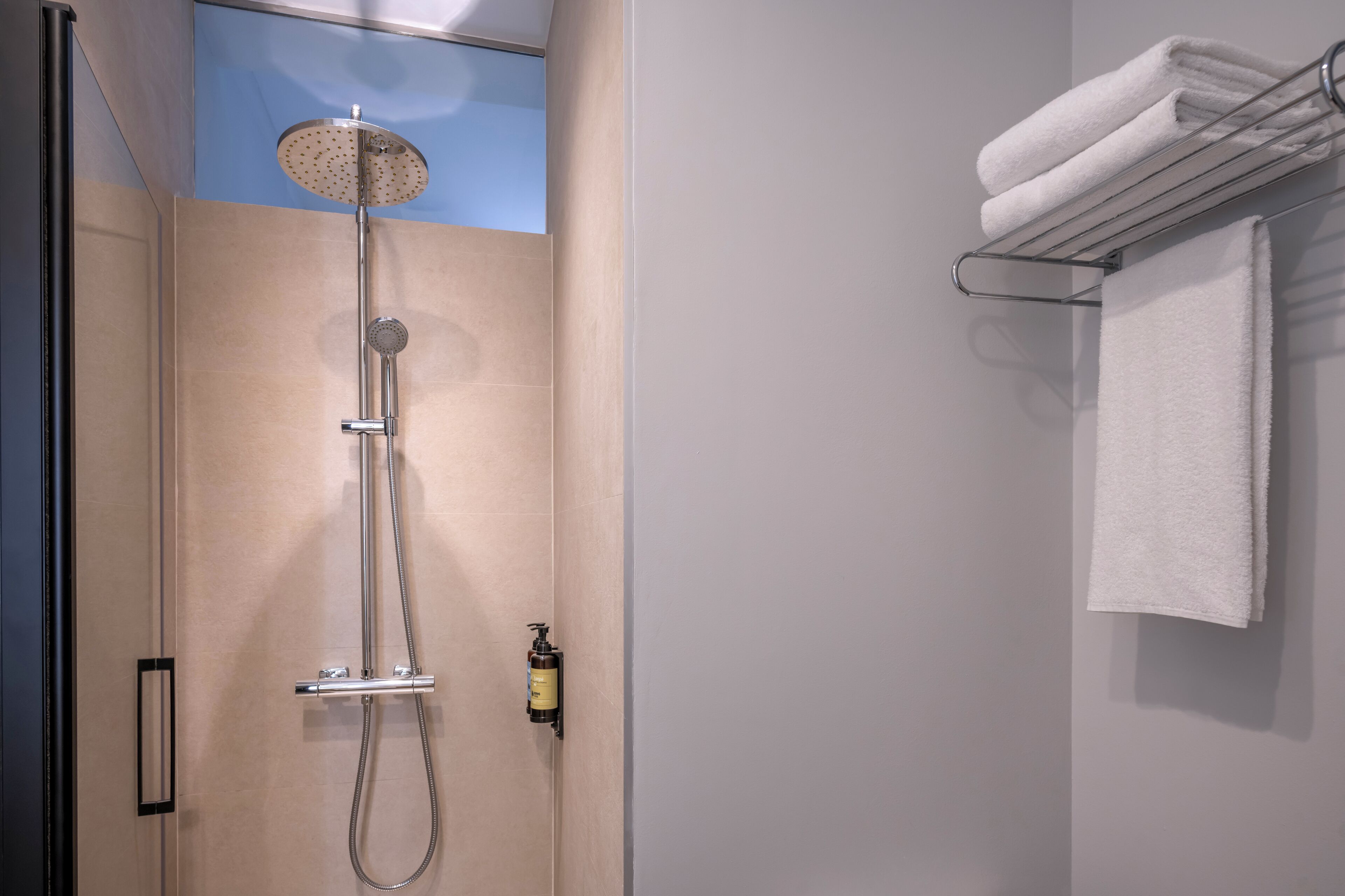 A modern bathroom with a shower, a towel rack, and a bottle of shampoo.