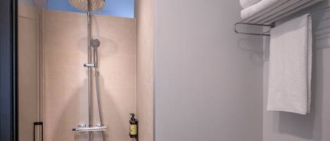 A modern bathroom with a shower, a towel rack, and a bottle of shampoo.
