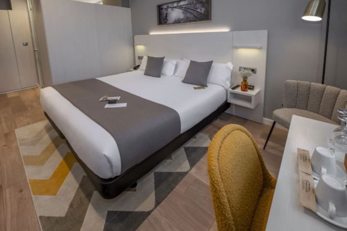 A modern hotel room with a large bed, bedside tables, a chair, and a dining area.