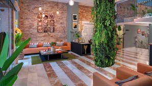 Un área de lounge moderna con pared de ladrillo, un amplio jardín vertical verde y un espacio de asientos con sofás naranja.