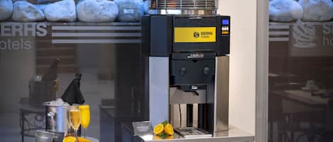 A coffee machine with a basket of oranges, a tray with two glasses of orange juice, and a sign for SerH's hotels.