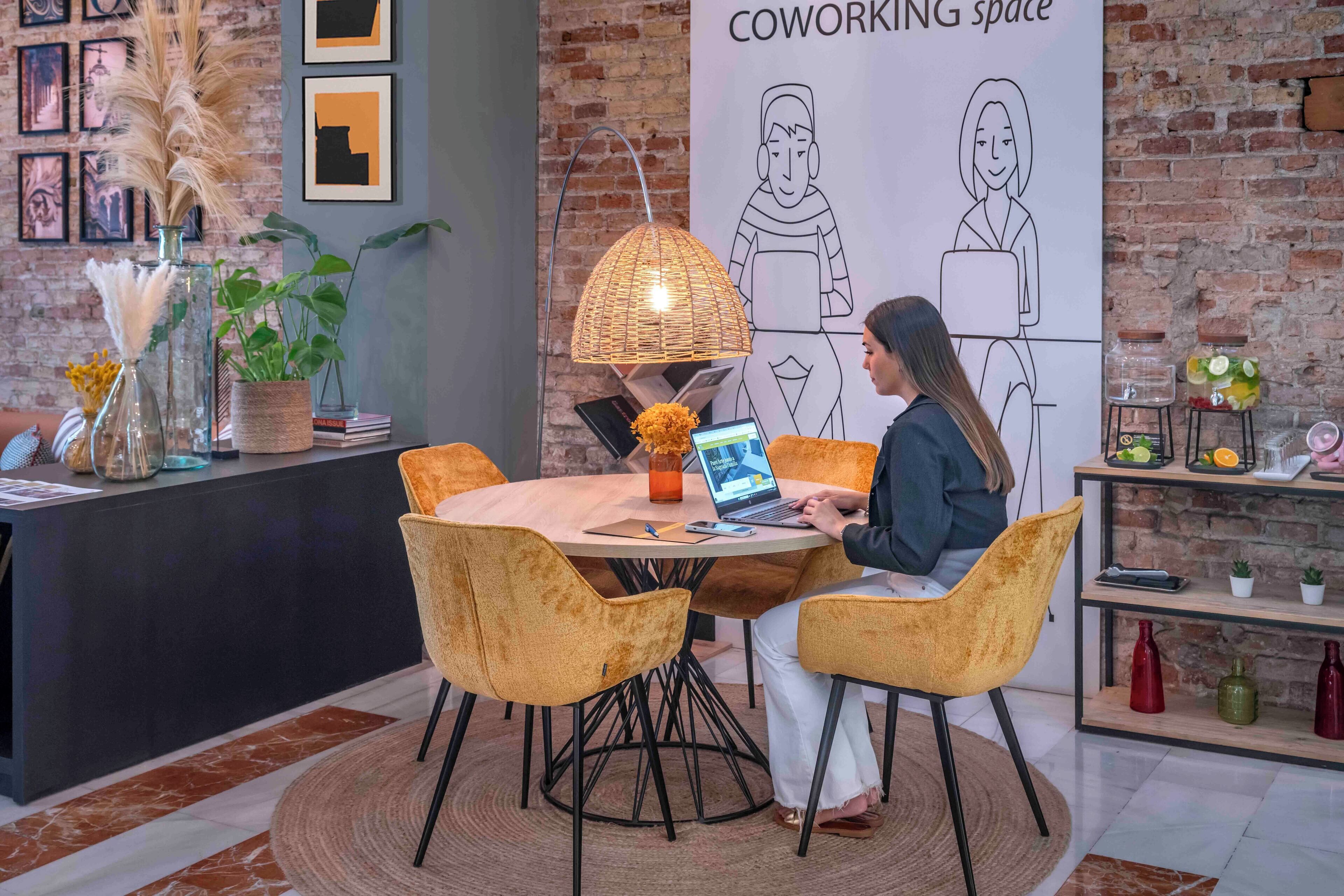 A coworking space with a round table, yellow chairs, a laptop, and a poster on the wall.
