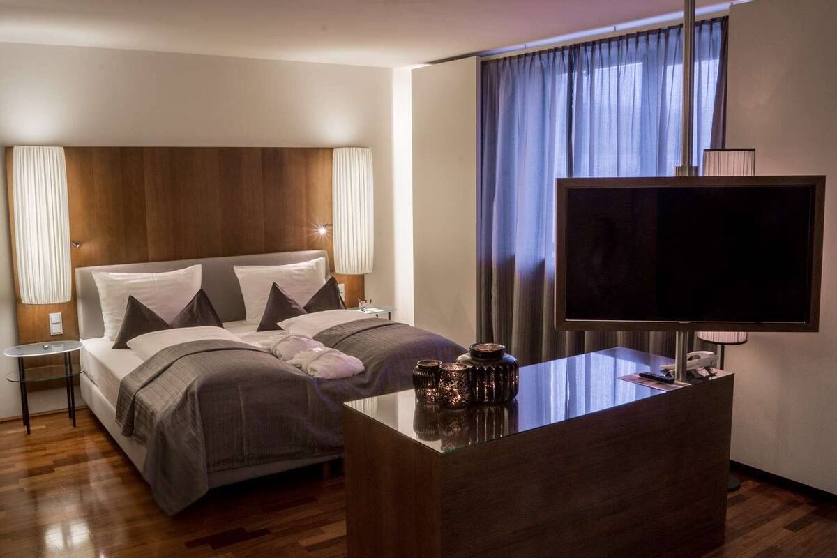 A hotel room with a large bed, a TV, a small table, and a desk with decorative items.