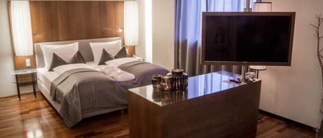 A modern hotel room with a large bed, a desk with a flat-screen TV, and a small side table.