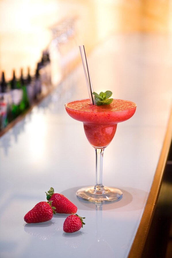 A cocktail in a martini glass with a straw and mint garnish, accompanied by three strawberries on a bar counter.