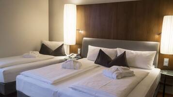 A hotel room with two beds, each with white linens and pillows, a wooden headboard, and bedside lamps.