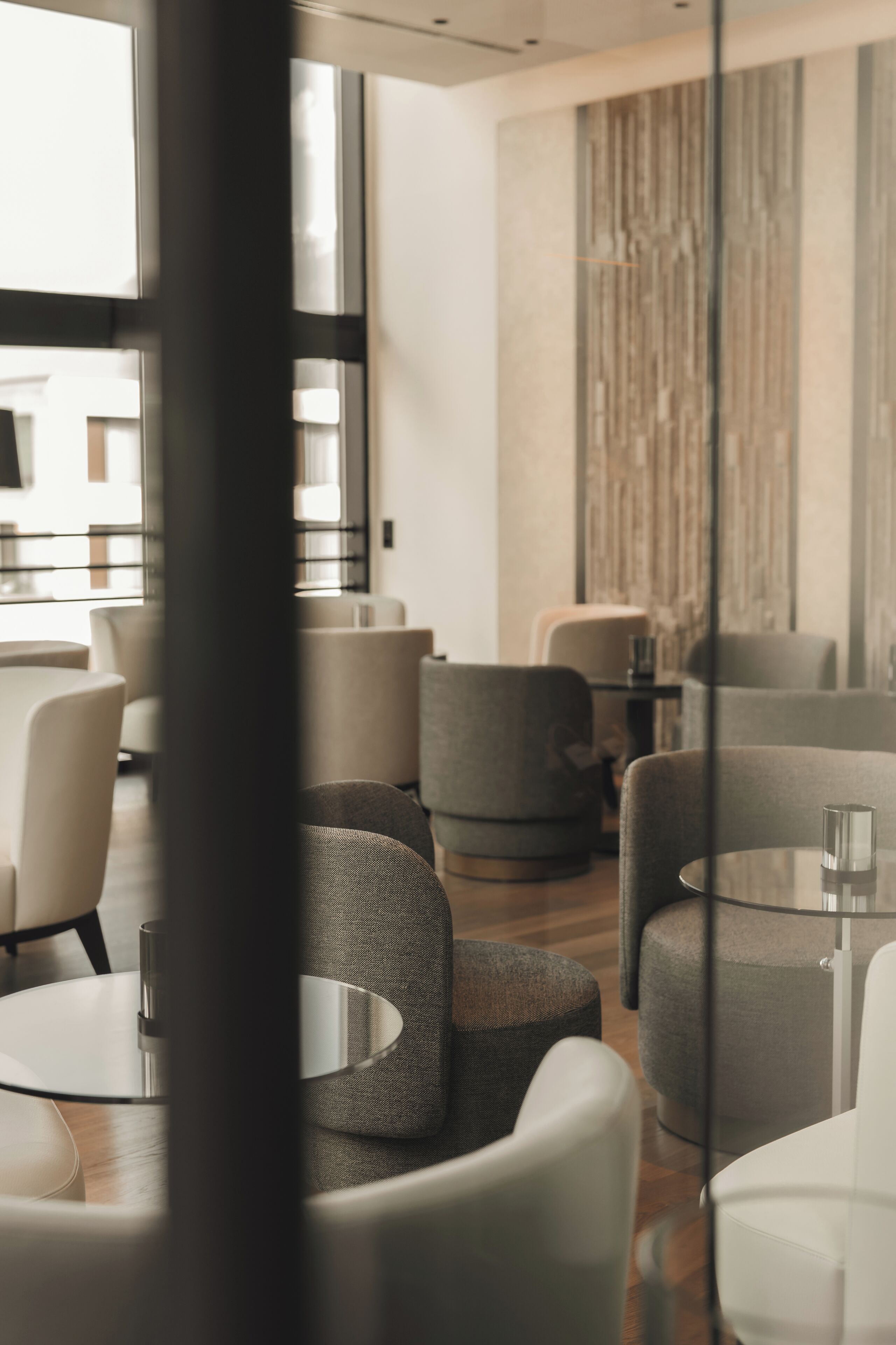 Un intérieur moderne avec des tables et des chaises rondes, une cloison en verre et une vue sur l’extérieur.
