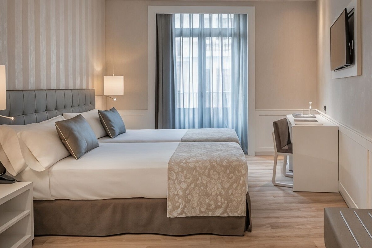 A hotel room with two beds, a desk, a chair, a television, and a window with curtains.