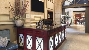 Ein Empfangsbereich mit einer Marmor-Theke, einer großen Vase mit Trockenpflanzen, einem Flachbildfernseher und Blick in die Lobby.
