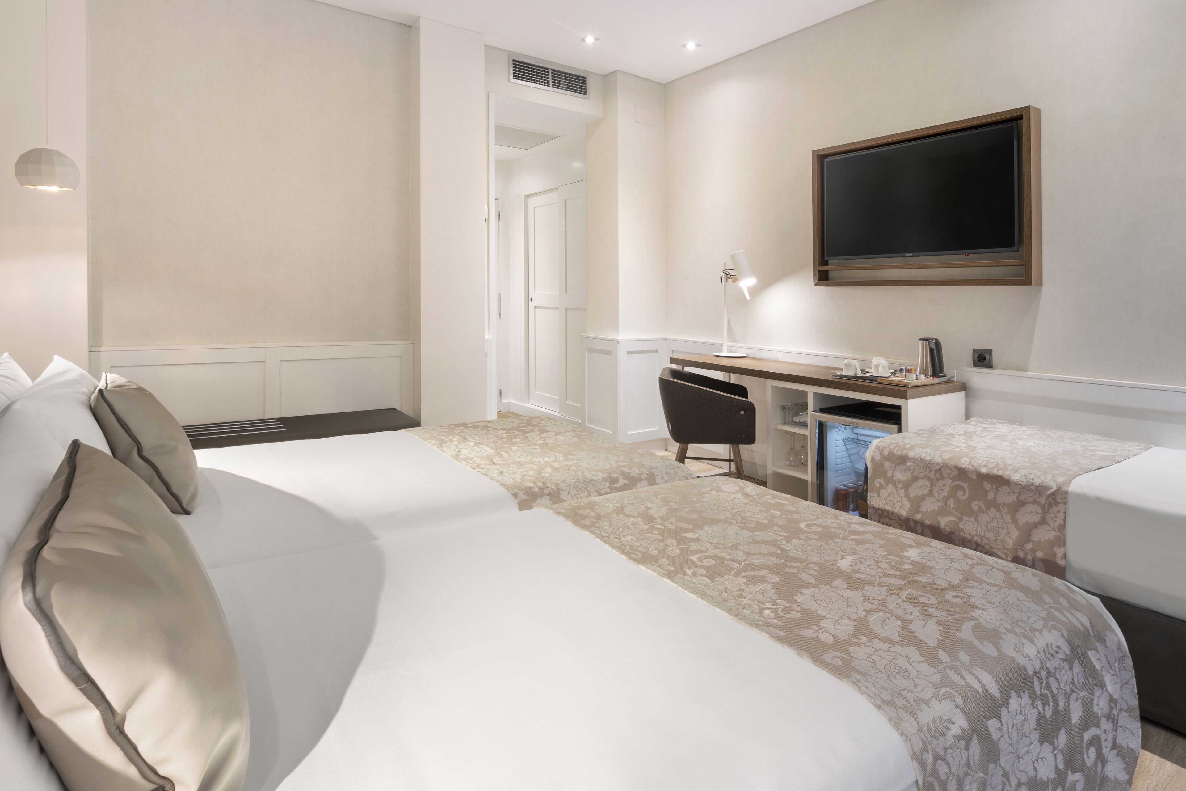 A hotel room with two beds, a desk, a television, and a coffee maker.