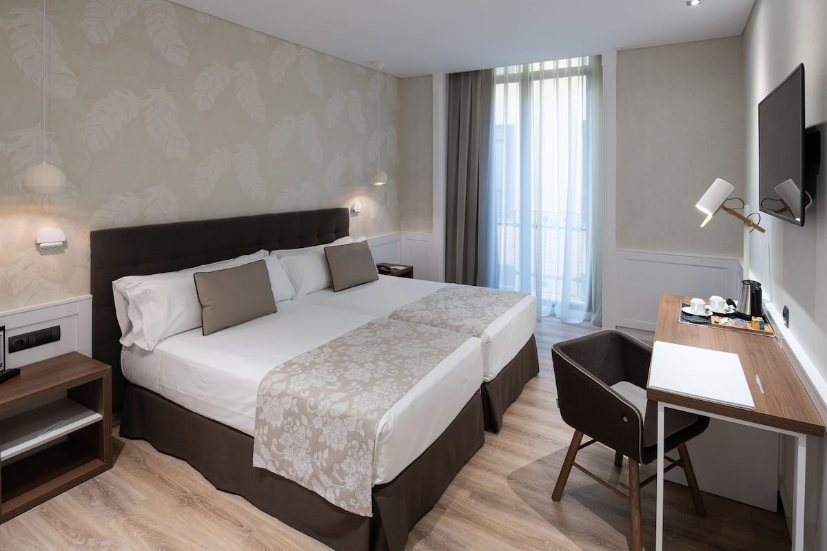 A modern hotel room with a large bed, a desk with a chair, a flat-screen TV, and a window with curtains.