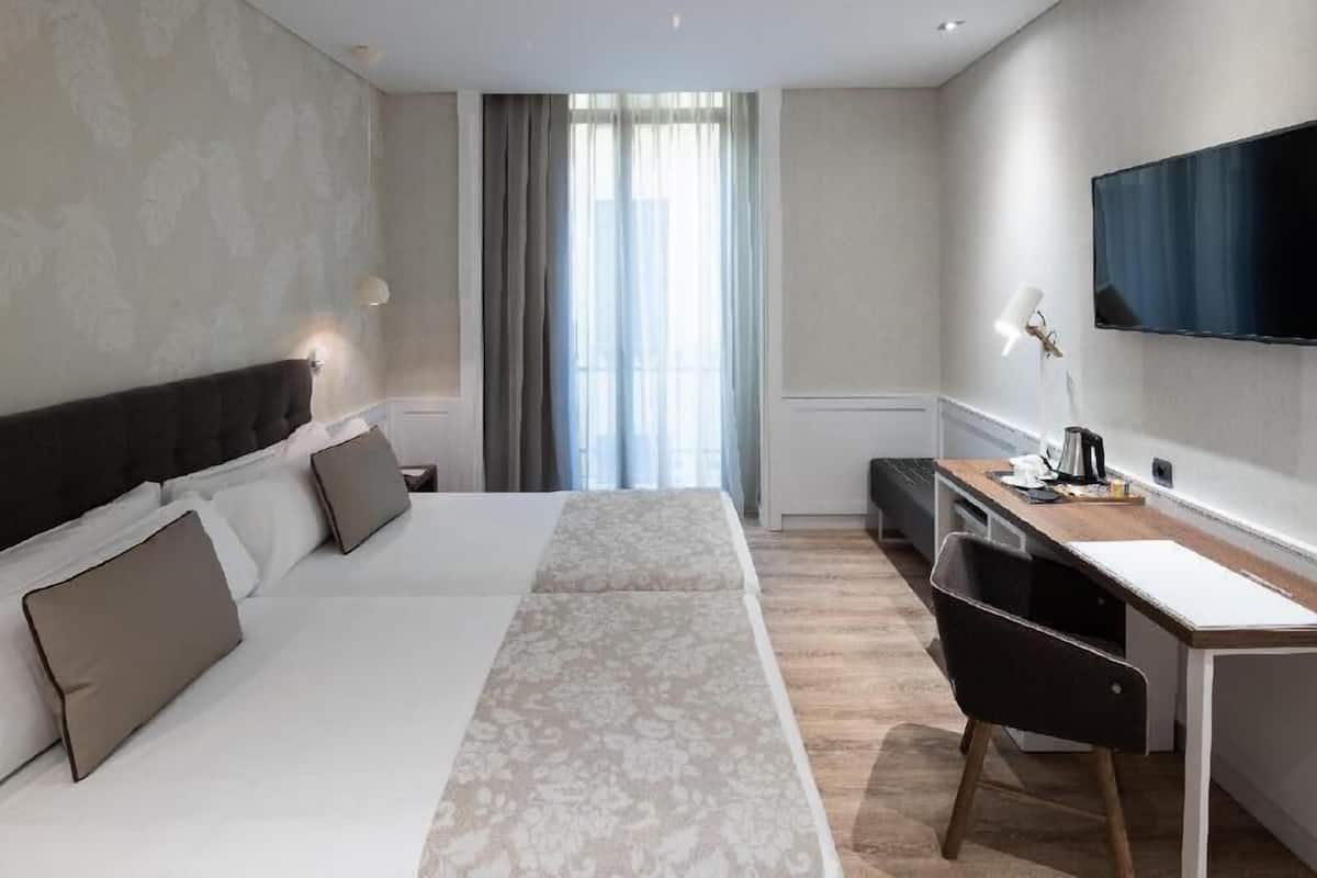 A hotel room with a bed, a desk, a chair, a TV, and a window with curtains.