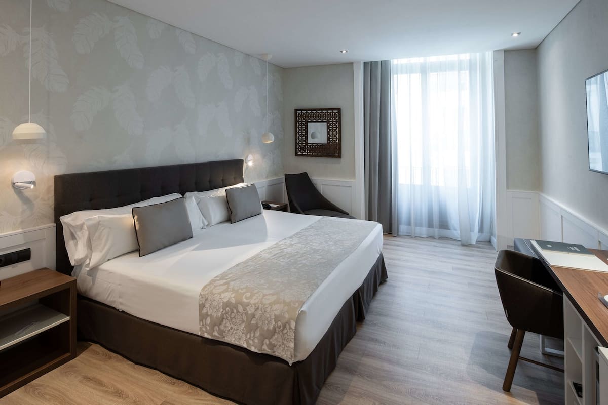 A modern hotel room with a large bed, bedside tables, a desk, and a chair.