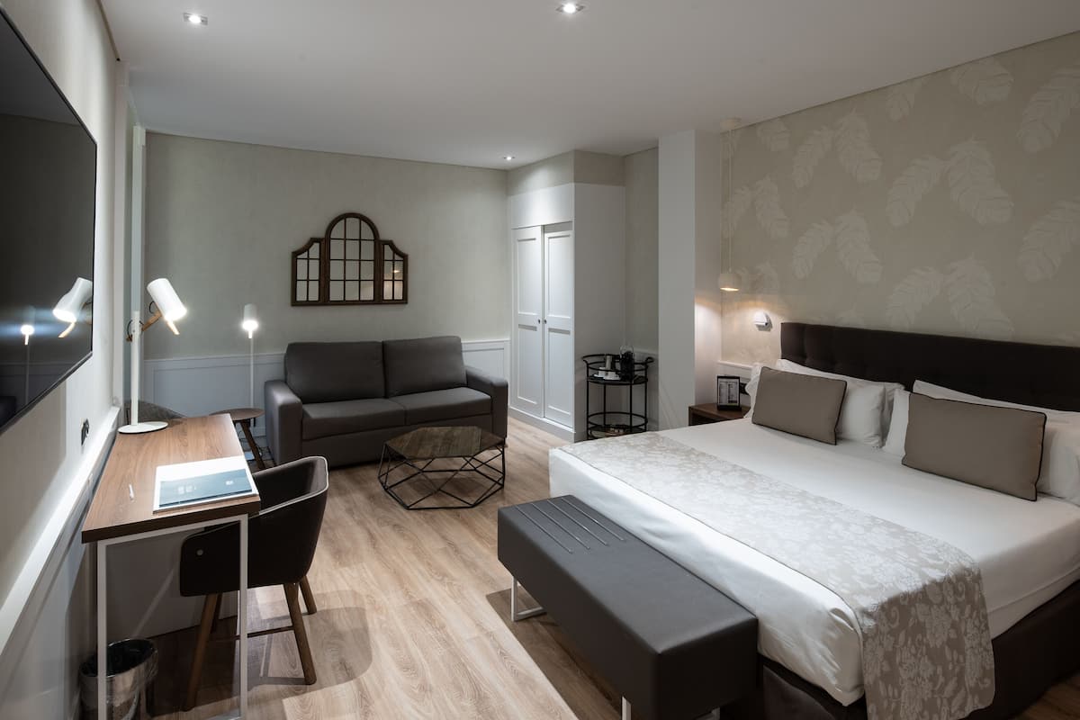 A modern hotel room with a bed, a desk, a sofa, and a small table.