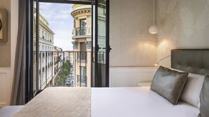 Ein Hotelzimmer mit einem großen Bett, Stadtblick vom Balkon und einer modernen Leuchte.
