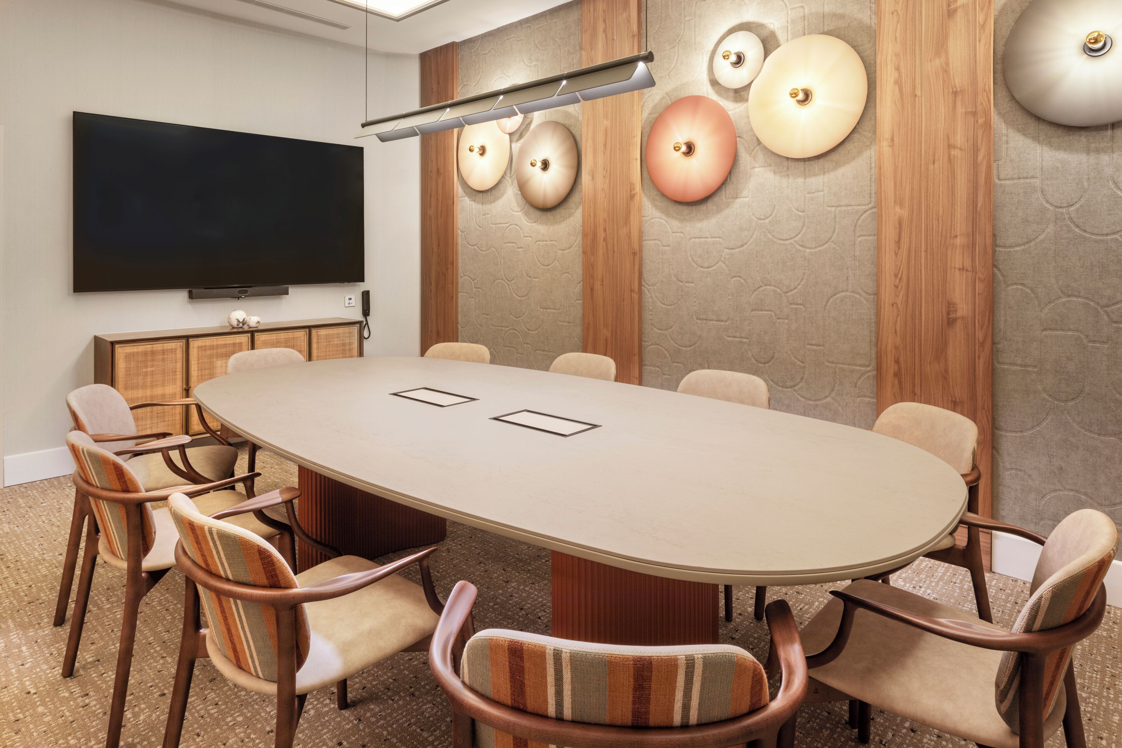 A conference room with a large oval table, six chairs, a flat-screen TV, and decorative wall panels.