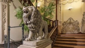 Eine prachtvolle Treppe mit einer Löwenstatue, aufwendigen Wandverzierungen und einem hölzernen Geländer.