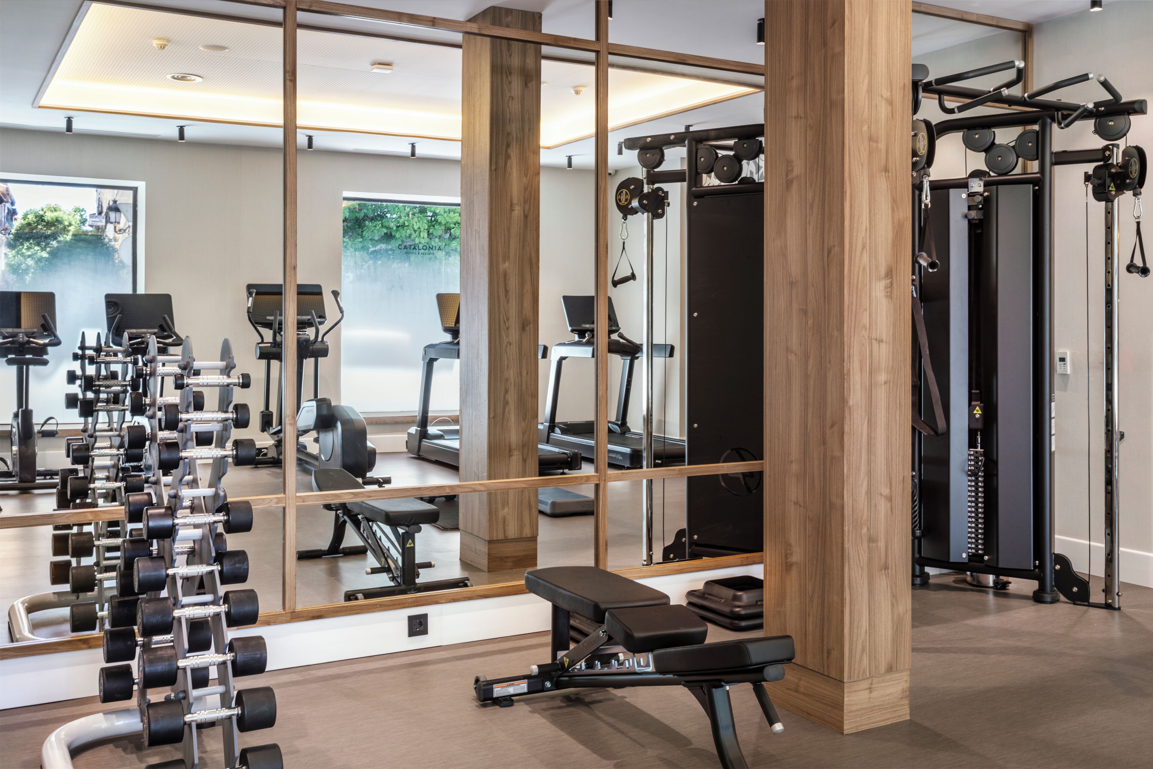 A gym with exercise equipment, mirrors, and a bench.