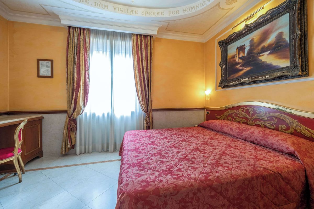 A hotel room with a large bed, a desk, and a painting on the wall.