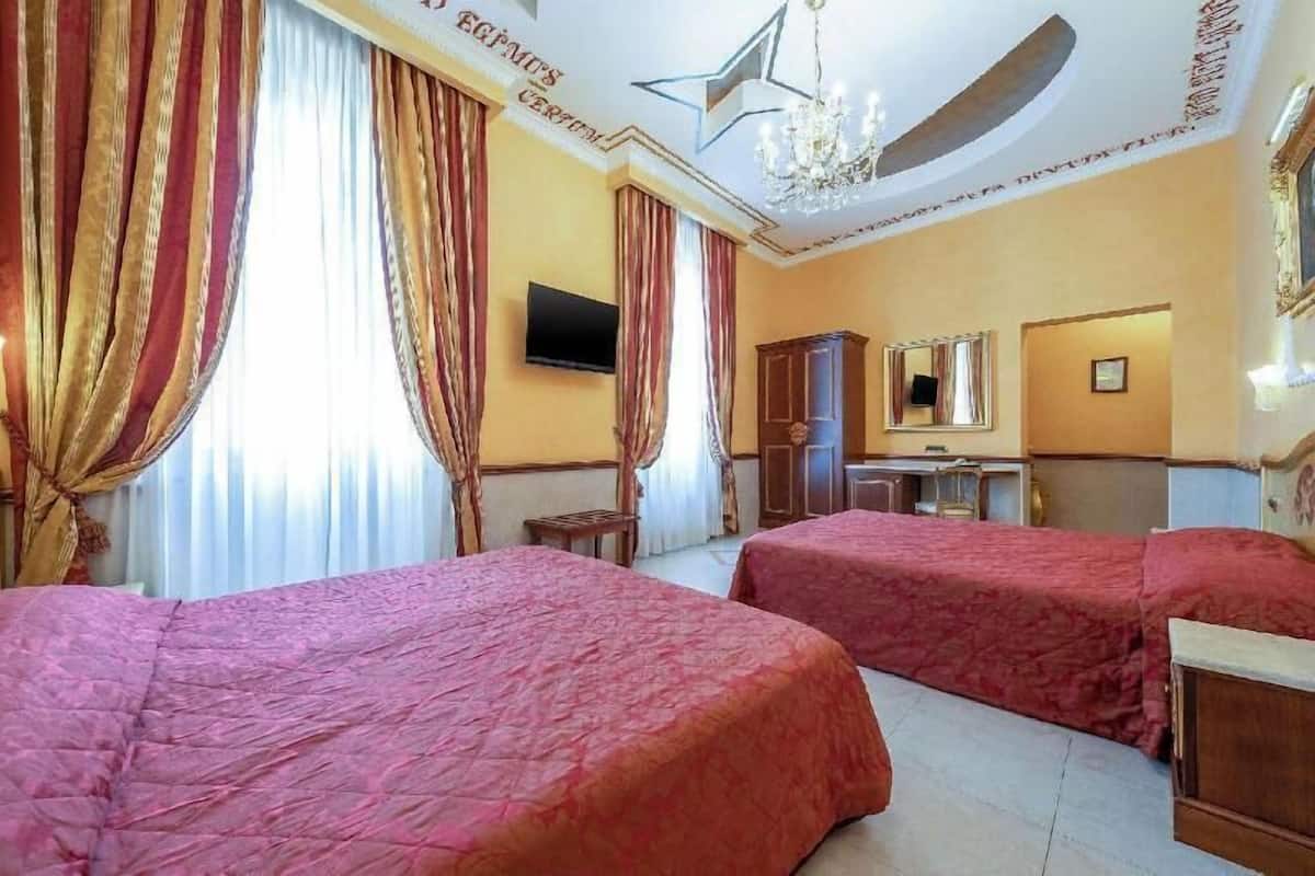 A hotel room with two beds, a TV, a mirror, and a chandelier.