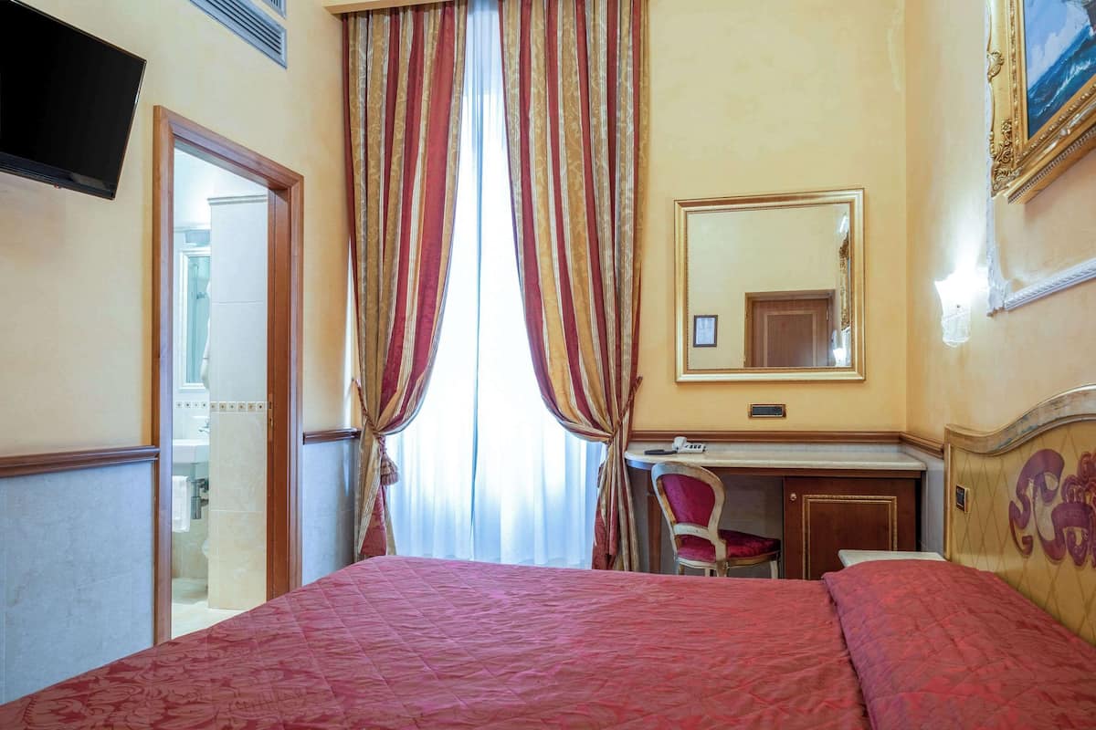 A hotel room with a bed, a desk, a chair, a mirror, and a television.