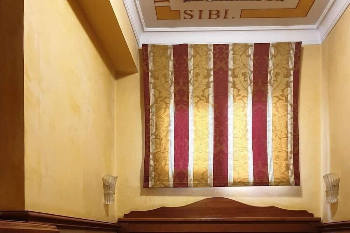 A single bed with a patterned bedspread, a wooden headboard, and a window with striped curtains.