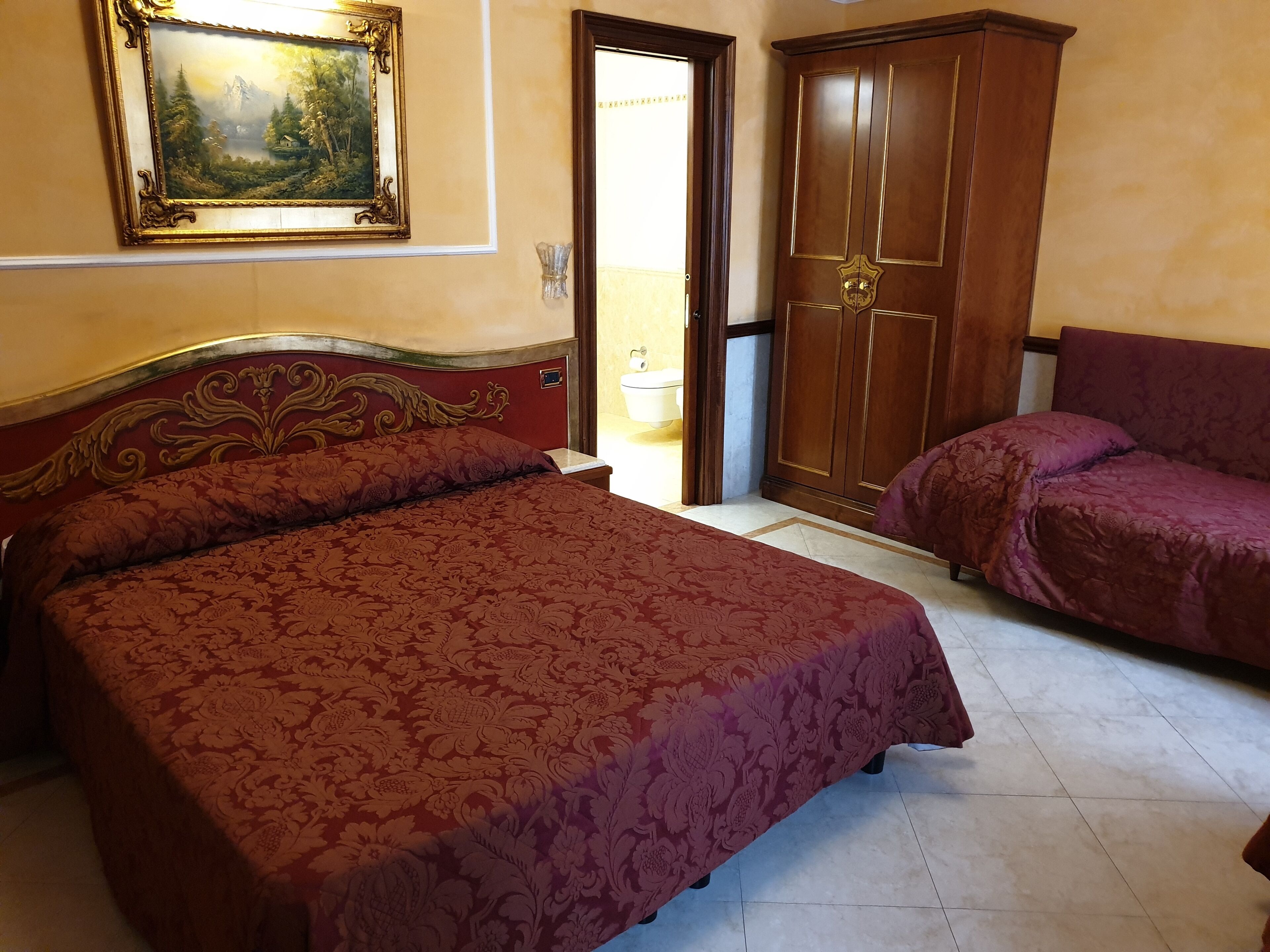 A bedroom with a large bed, a smaller sofa, a wardrobe, and a painting on the wall.
