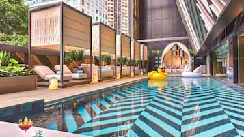 Piscina interior moderna com padrões geométricos em azulejos, áreas de estar com assentos e boias de cisne decorativas.