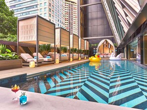 Una piscina interior moderna con diseños geométricos en los azulejos, zonas de estar con asientos y flotadores decorativos con forma de cisne.