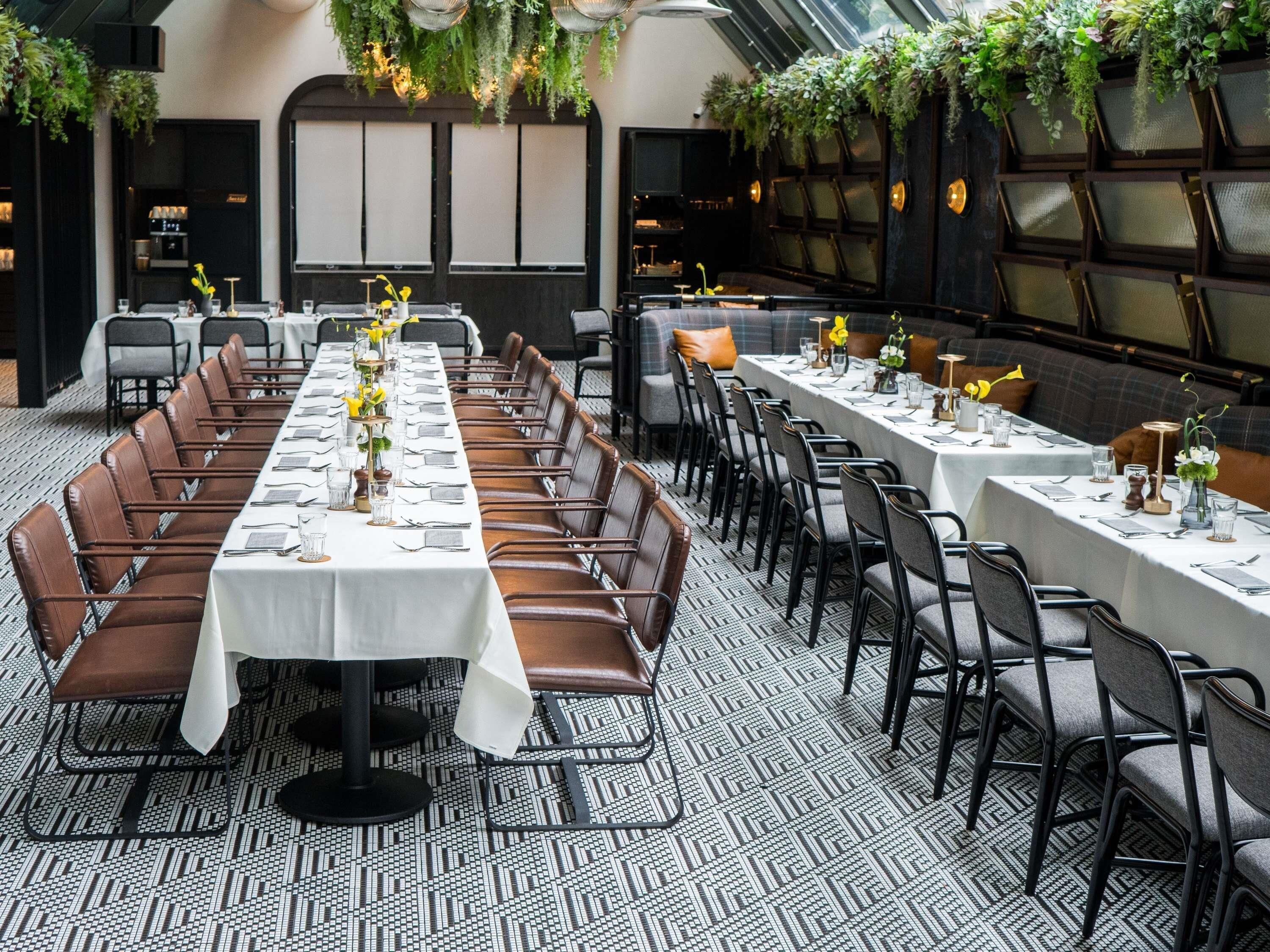 Una larga mesa de comedor con sillas, piso estampado y plantas colgantes.