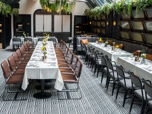 A long dining table with chairs, a patterned floor, and hanging plants.