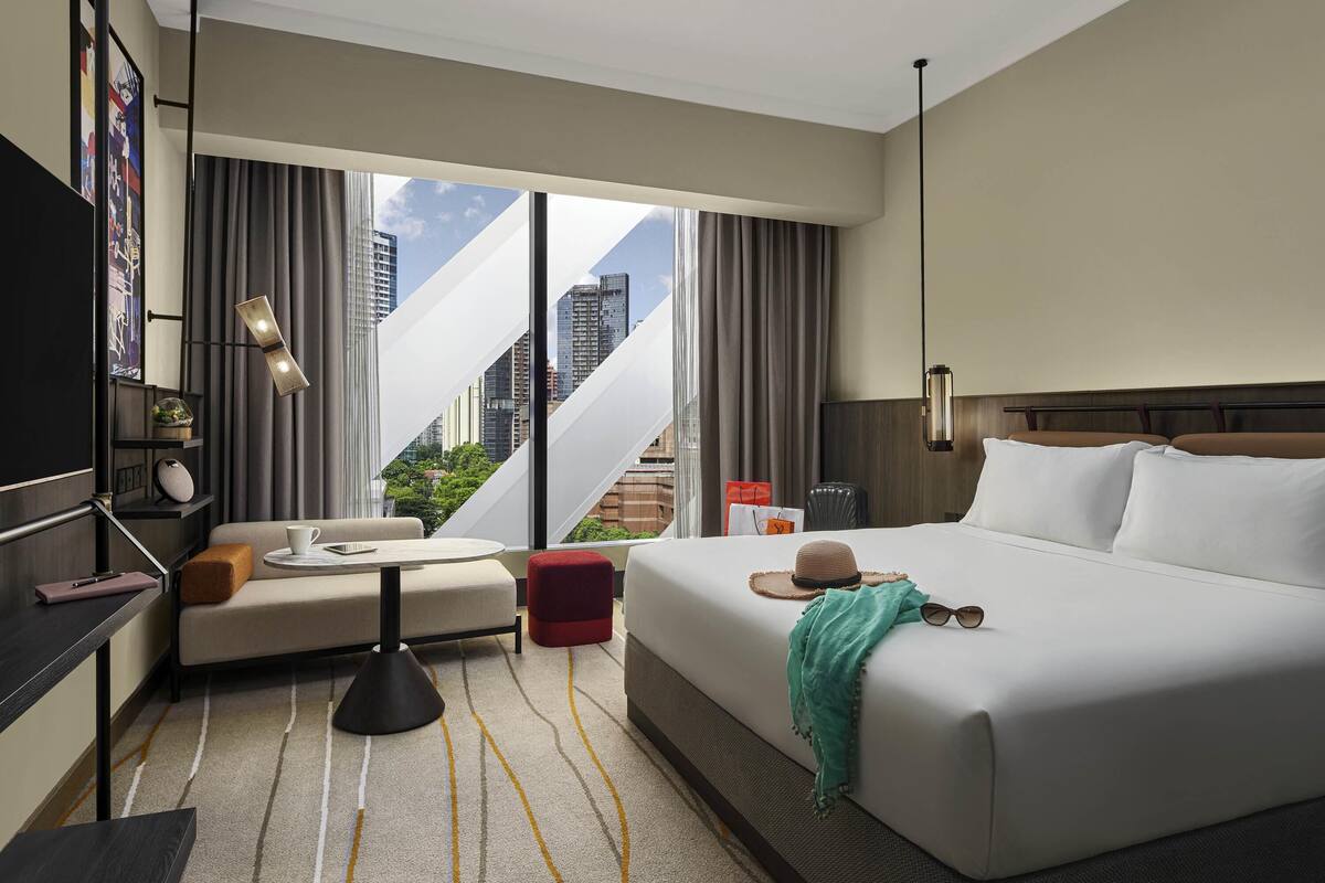 Habitación de hotel con cama, sofá, una mesita, televisor y vistas a la ciudad.