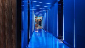 Un pasillo moderno iluminado en azul con un suelo reflectante, que conduce a una zona de recepción.
