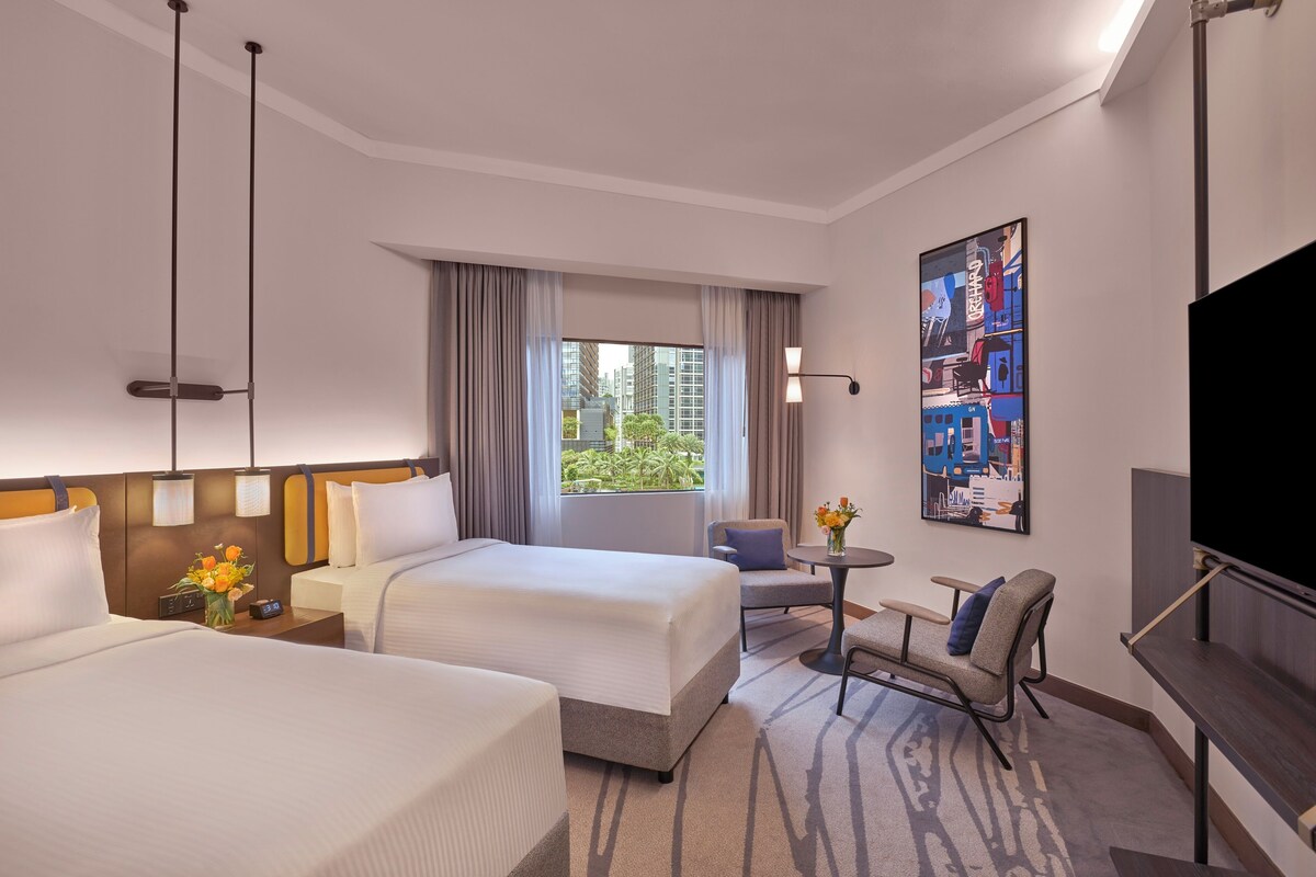 Habitación de hotel con dos camas, televisión, una mesita con un florero y una ventana con cortinas.