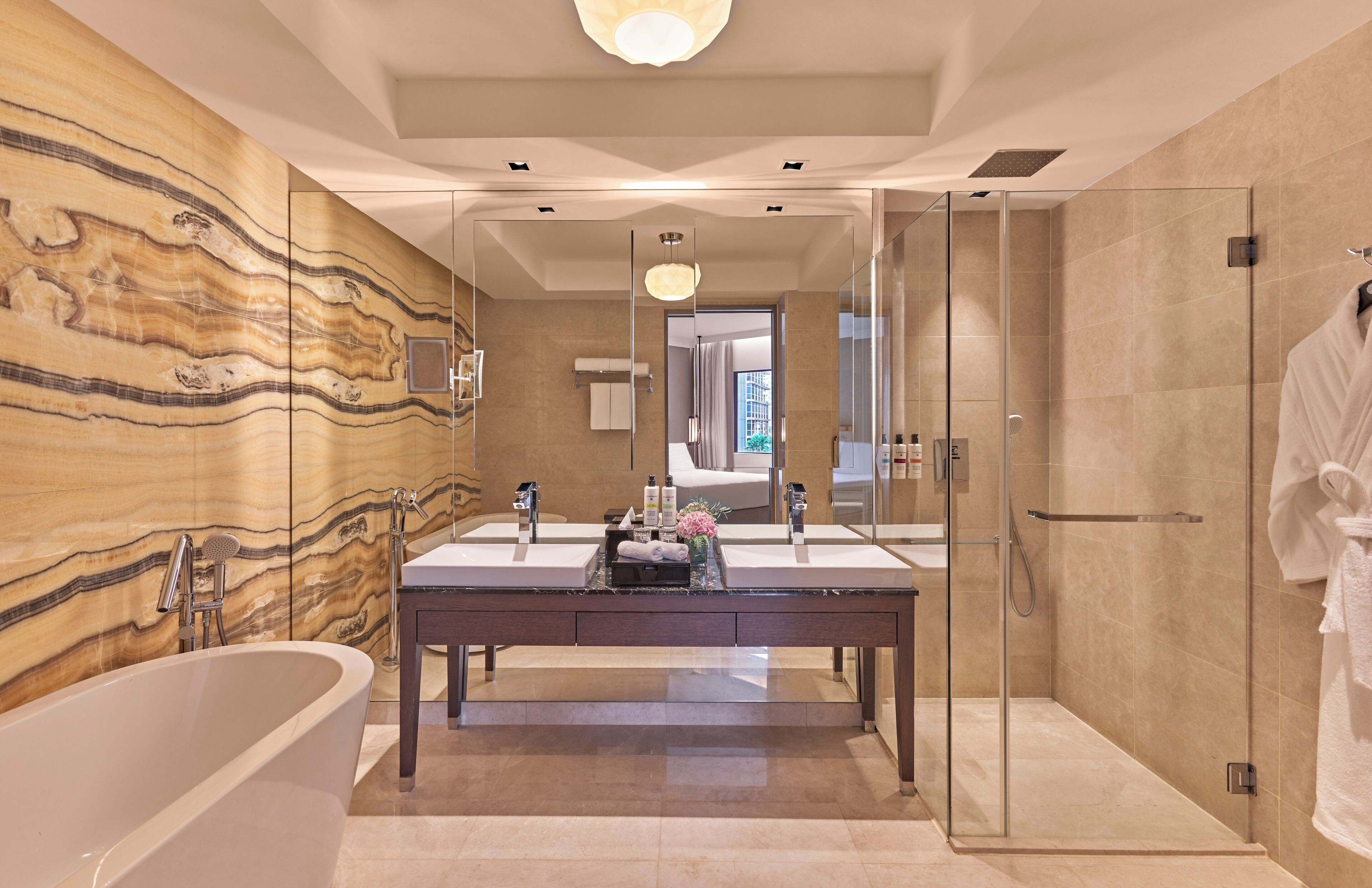 A modern bathroom with a marble wall, a freestanding bathtub, and a glass-enclosed shower.