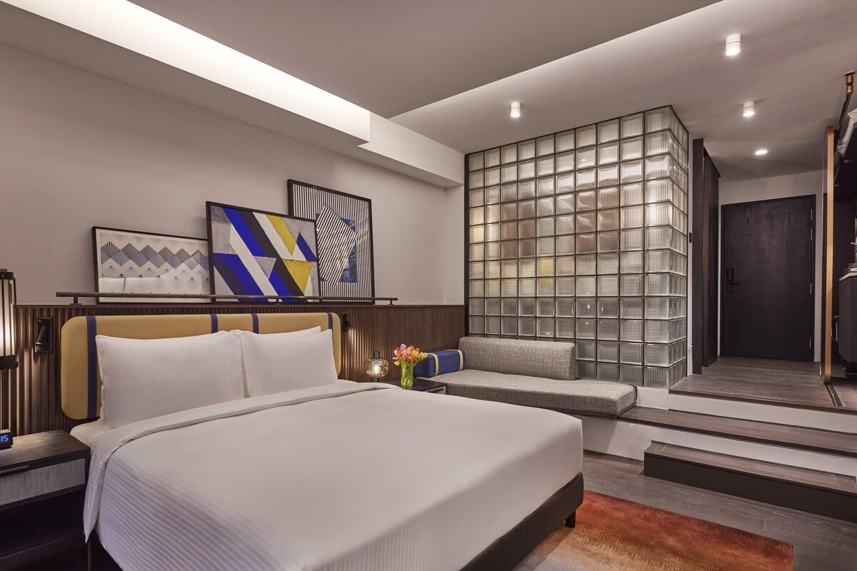 Una habitación de hotel moderna con una cama grande, un área de descanso y un muro decorativo.