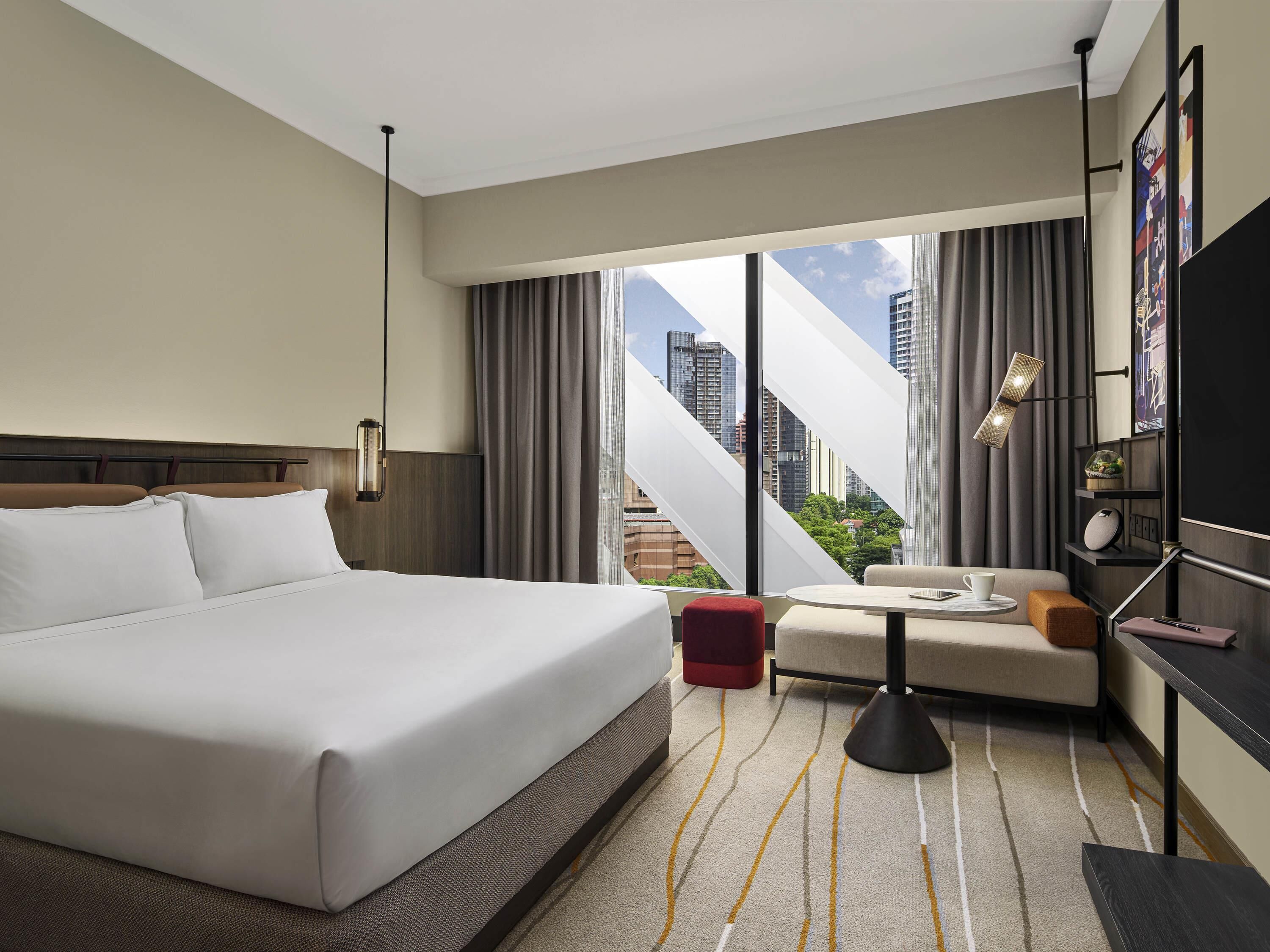Une chambre d’hôtel avec un grand lit, un canapé, une petite table, une lampe et une vue sur le paysage urbain.