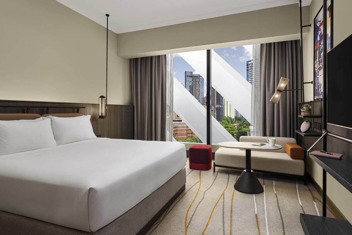 Una habitación de hotel con una cama grande, un sofá, una mesita, una lámpara y vistas a la ciudad.